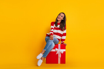 Fototapeta na wymiar Full length photo of an excited beautiful stylish brunette woman while she is sitting and posing with a big red gift box