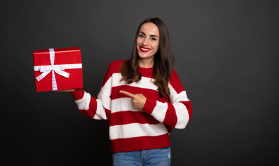 Beautiful smiling modern young girl with gift box in hand is pointing on present