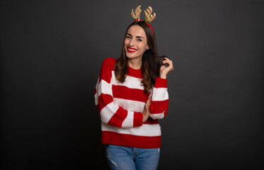 Close up photo of a beautiful smiling trendy woman with Сhristmas reindeer antlers on her head while she posing and having fun and isolated on gray background