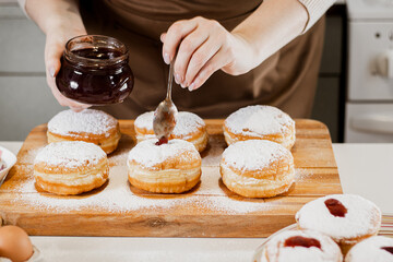 Woman chef prepares fresh donuts with jam at her bakery. Cooking traditional Hanukkah sufganiyot. Small business.