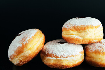 Powdered sugar is poured onto donuts. Traditional Jewish dessert Sufganiyot on black background. Cooking fried Berliners.