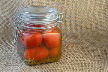 homemade pickled tomatoes in a glass jar on burlap cloth