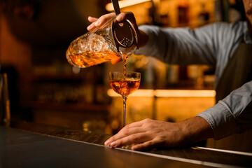 view of mixing cup with cold cocktail and strainer from which the beverage is poured into a wine glass