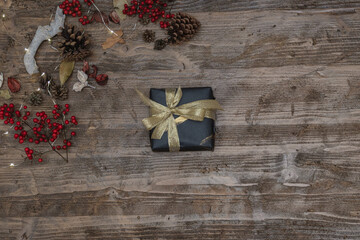Flat lay of a christmas gift on a wooden surface with pine cones, red berries and led lights