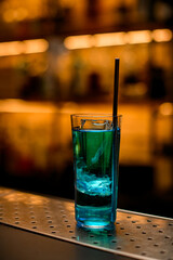 Close-up of glass of bright blue cocktail with piece of ice and steel drinking straw
