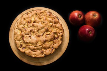 Apple pie on a dark background with three red apples