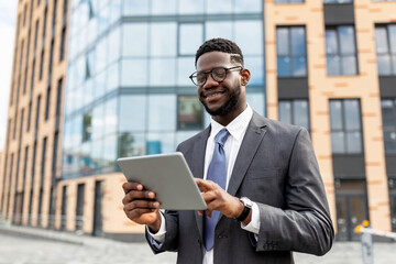 Fototapeta premium Confident black businessman with tablet outdoors. Insuranse agent browsing news on digital device, walking outdoors