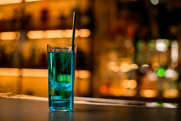 selective focus of glass of bright blue cocktail with piece of ice and steel drinking straw