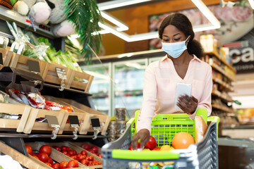 Black Lady Shopping Groceries Using Phone In Supermarket, Wearing Mask