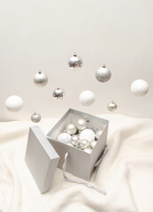 Silver Christmas tree baubles falling in grey present box on white background. Creative composition for New Year giving.