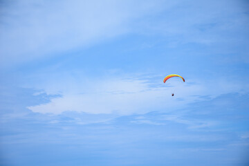 One paraglider with a red yellow parachute against a vibrant blue cloudy sky