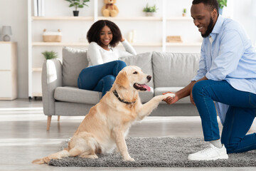 Smiling black man playing with dog in the living room