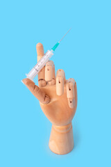 Syringe and wooden hand on blue background, Vaccination concept