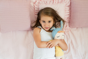 The girl is lying in bed hugging a toy doll before going to bed. Children's sleep and wake mode....
