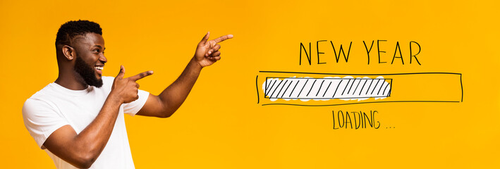 Positive African American guy pointing both hands aside at New Year loading progress bar over orange background