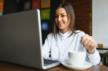 Portrait of a young female freelancer using laptop computer for distance job while sitting in...