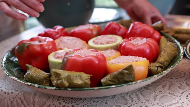 People hands are preparing food. Peppers, tomatoes, zucchini and grape leaves stuffed with minced meat.