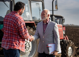 Farmer and insurance person shaking hands in field