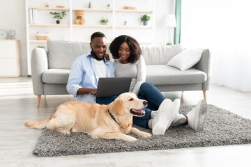 Black couple at home using laptop relaxing with dog