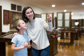 Smiling woman with school age son visiting museum together pointing to something interesting