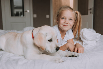 portrait of a little blonde girl lying in bed with her beloved dog in her arms. girl in a white T-shirt and jeans and a pet are lying on white bed linen. space for text. High quality photo