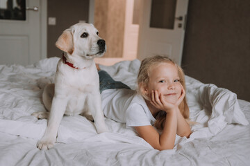 portrait of a little blonde girl lying in bed with her beloved dog in her arms. girl in a white T-shirt and jeans and a pet are lying on white bed linen. space for text. High quality photo
