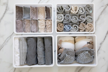 Womans underwear, pajamas and socks neatly folded and placed in closet organizer drawer divider on white marble table.
