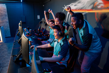 Multiracial team of happy professional cyber sports gamers celebrating success wile raising hands...