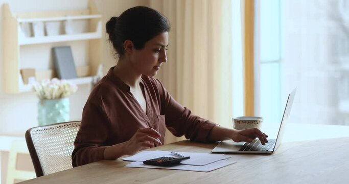 Reviewing finances. Indian female housewife manage family budget pay bills using digital calculator to check financial data on pc before paying. Millennial woman plan monthly loan mortgage payments