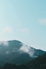 Fototapeta premium Clouds covering green mountain with blue skies