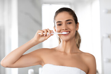Headshot Of Lady Brushing Teeth Looking At Camera In Bathroom