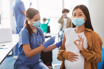 Vaccinated Pregnant Asian Lady Gesturing Okay Sign At Clinic