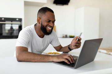 Black man using pc and smartphone having breakfast at home