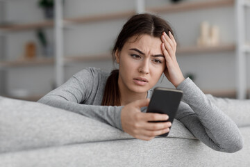 Sad frustrated shocking european young woman suffering from depression and reading message with bad...