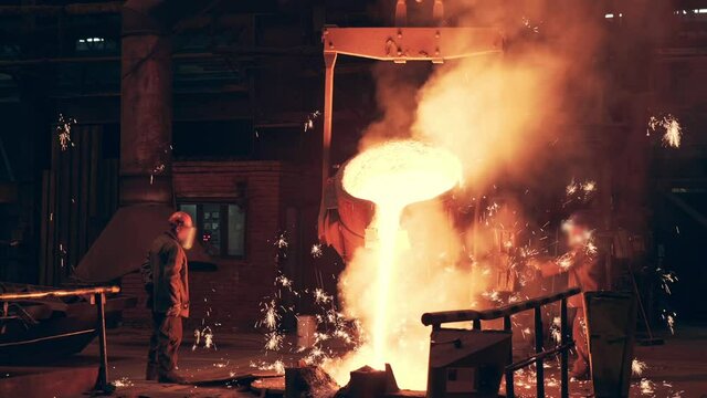 Blast furnace in foundry metallurgical factory. Pouring bright hot liquid steel or metal. Iron smelting process with bright sparks and smoke.