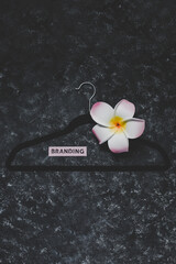 fashion industry and shopping trends, velvet clothes hanger on black background with Branding label and decorative flowers