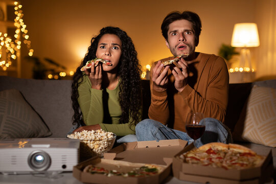 Shocked Couple Watching Horror Movie And Eating Pizza Sitting Indoors