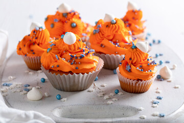 Delicious orange cupcakes with blue sprinkles and cream.