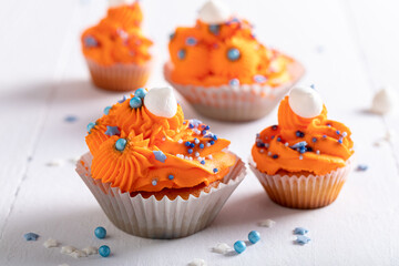 Sweet orange cupcakes with blue sprinkles and cream.