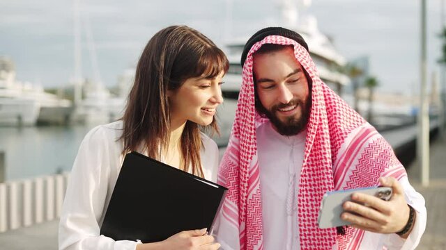 Smiling arab businessman showing something on smartphone to his attractive european female assistant