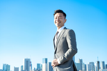 青空とビル群を背景にしたビジネスマンのポートレート