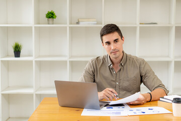 Fototapeta premium Businessman working with marketing graphs and laptop in online working concept with financial documents and analytical calculators while sitting in the office.