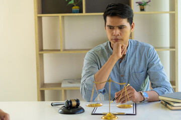 Asian male lawyer working on legal contract documents in a courtroom of justice. and legal concepts In the office with hammers and scales on the table