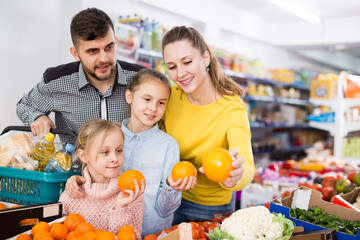 Fototapeta premium Young parents with two girls choosing sweet citrus fruits in food store