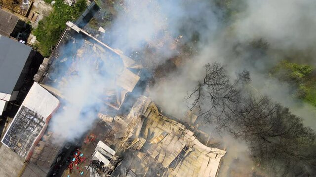 Aerial view of ruined building on fire with collapsed roof and rising dark smoke
