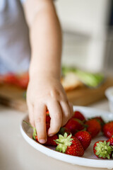 Closeup hand cute little baby taking fresh red berry strawberry from plate seasonal harvest