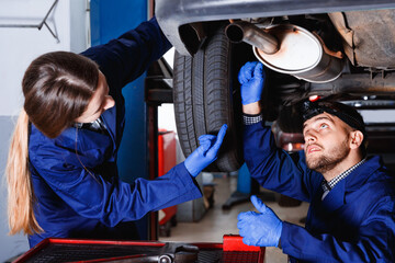 Two glad cheerful masters are repairing car in workshop.