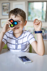 Portrait smiling boy fooling covering eye with simple dimple popit toy posing sitting at table