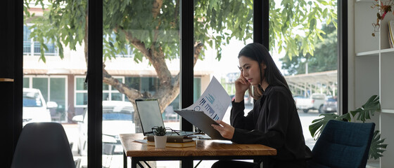 Side view young asian businesswoman sitting on her workplace in the office. Young woman working for...