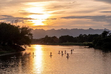 Naklejka na ściany i meble Stand-up paddleboarders in the River Kwai in Thailand at sunset